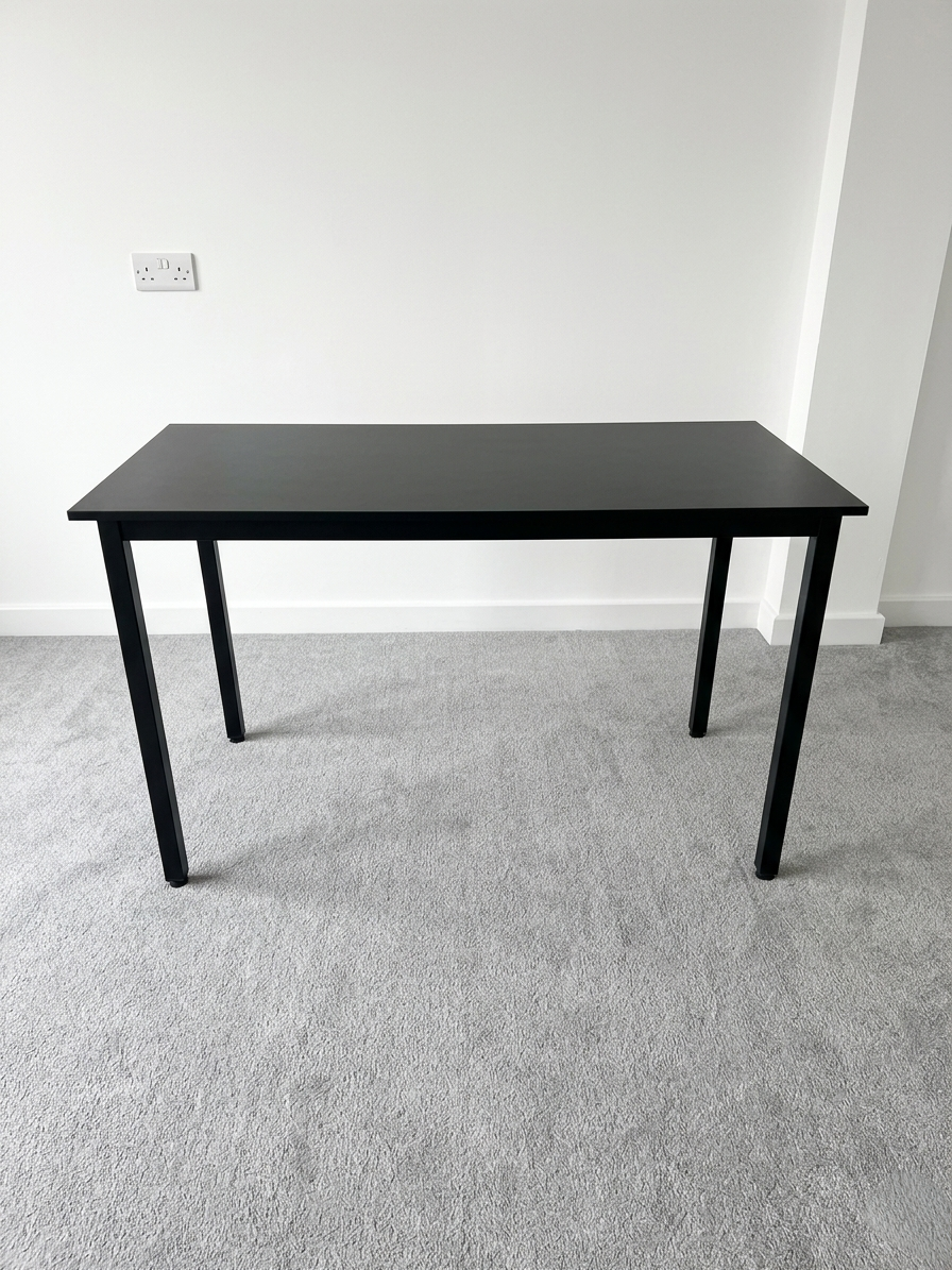 Black table on a gray carpeted floor with a white wall background
